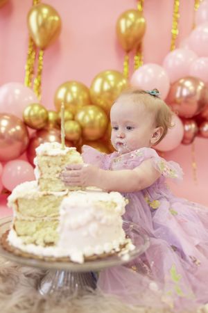 Baby in purple tutu dress smashing and playing with birthday cake during first birthday cake smash photoshoot.