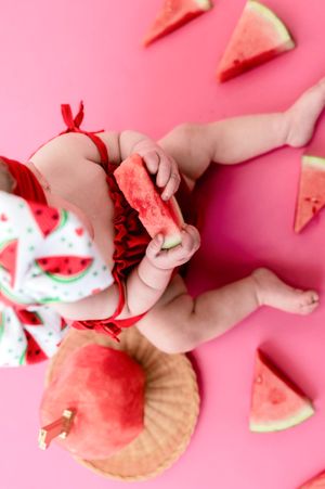 Hands arranging pieces of fresh watermelon on a pink background in a creative flat lay composition.