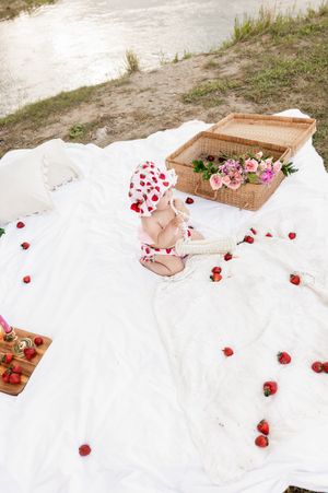 Outdoor picnic setup with wicker basket and scattered red rose petals on white blanket.