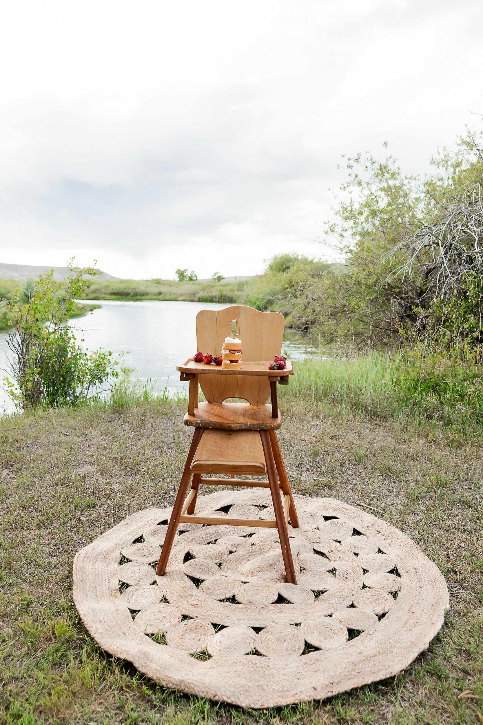 Wooden high chair placed on circular patterned rug in outdoor natural setting.