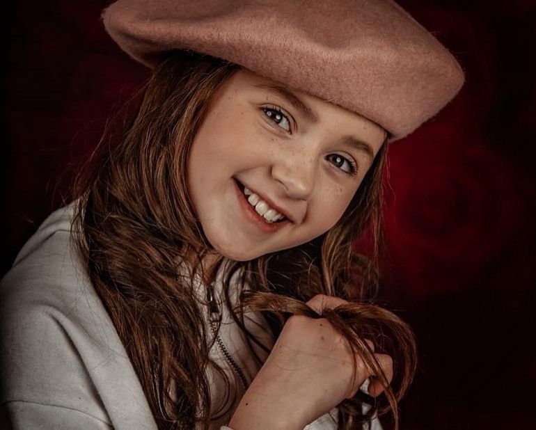Portrait against dark red background with dramatic lighting and warm tones.