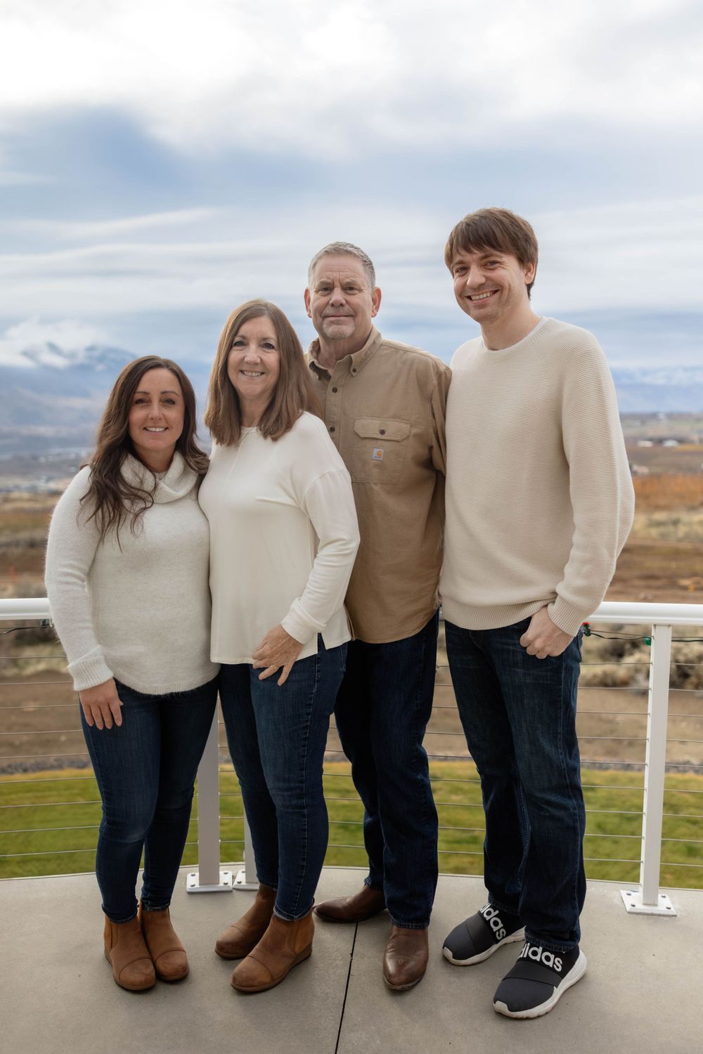 Family wearing coordinated cream and tan sweaters posing on outdoor deck with mountain views.