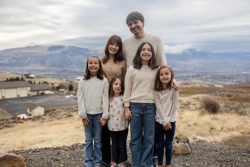 Family portrait taken outdoors with desert mountains and cloudy sky in the background.