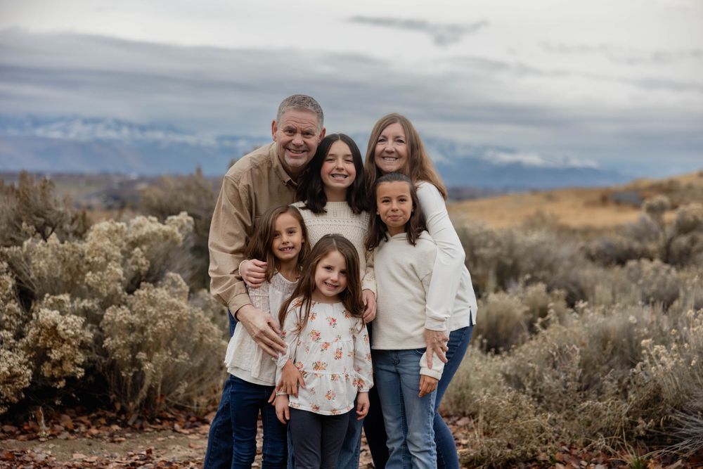 Family group poses for a casual portrait in a natural desert setting with mountains behind them.