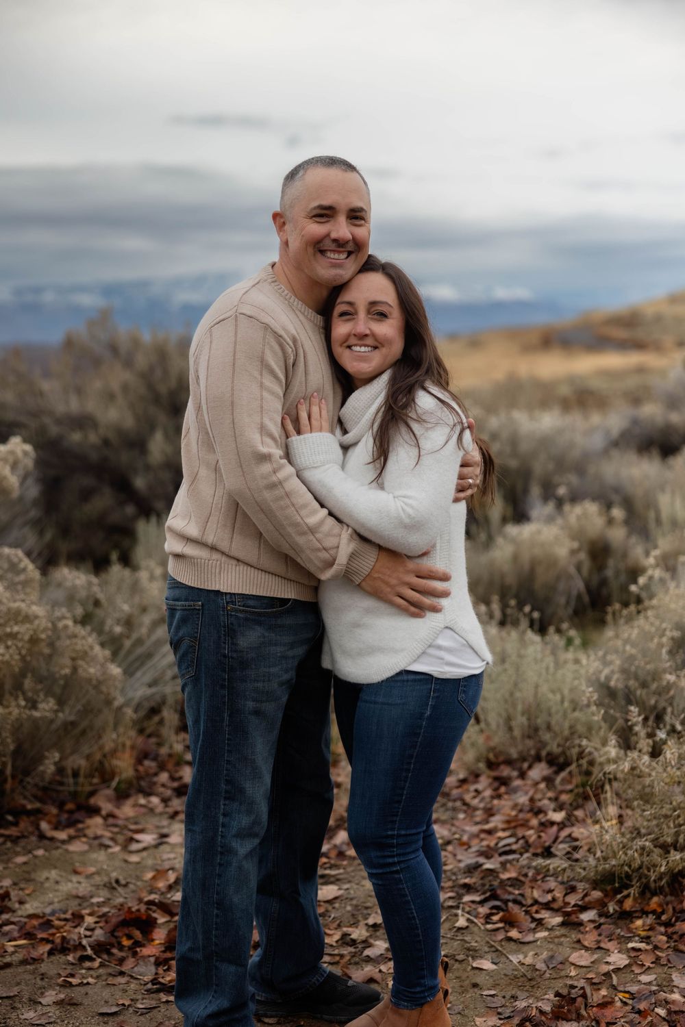 A couple embraces while wearing neutral sweaters against a desert backdrop.