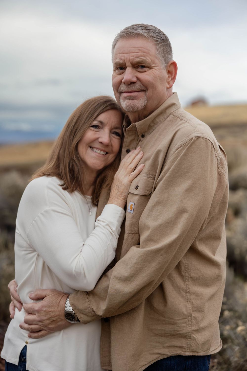 A couple in casual attire shares an intimate moment outdoors against a desert landscape.