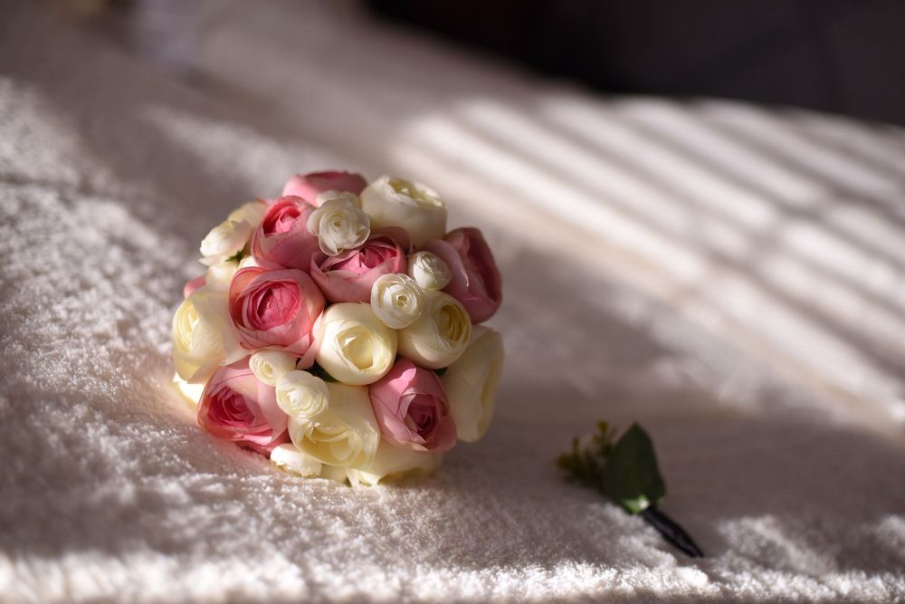 Wedding bouquet of pink and cream roses lying on white fabric in soft natural lighting.