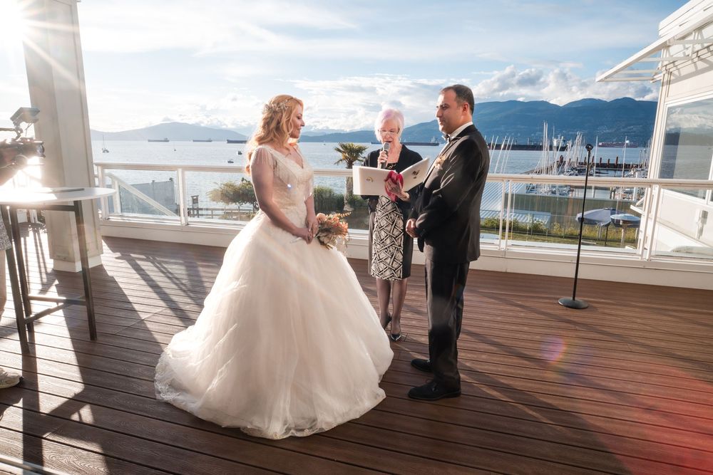 A wedding couple dances together on a scenic waterfront deck with mountains and water views in the background.