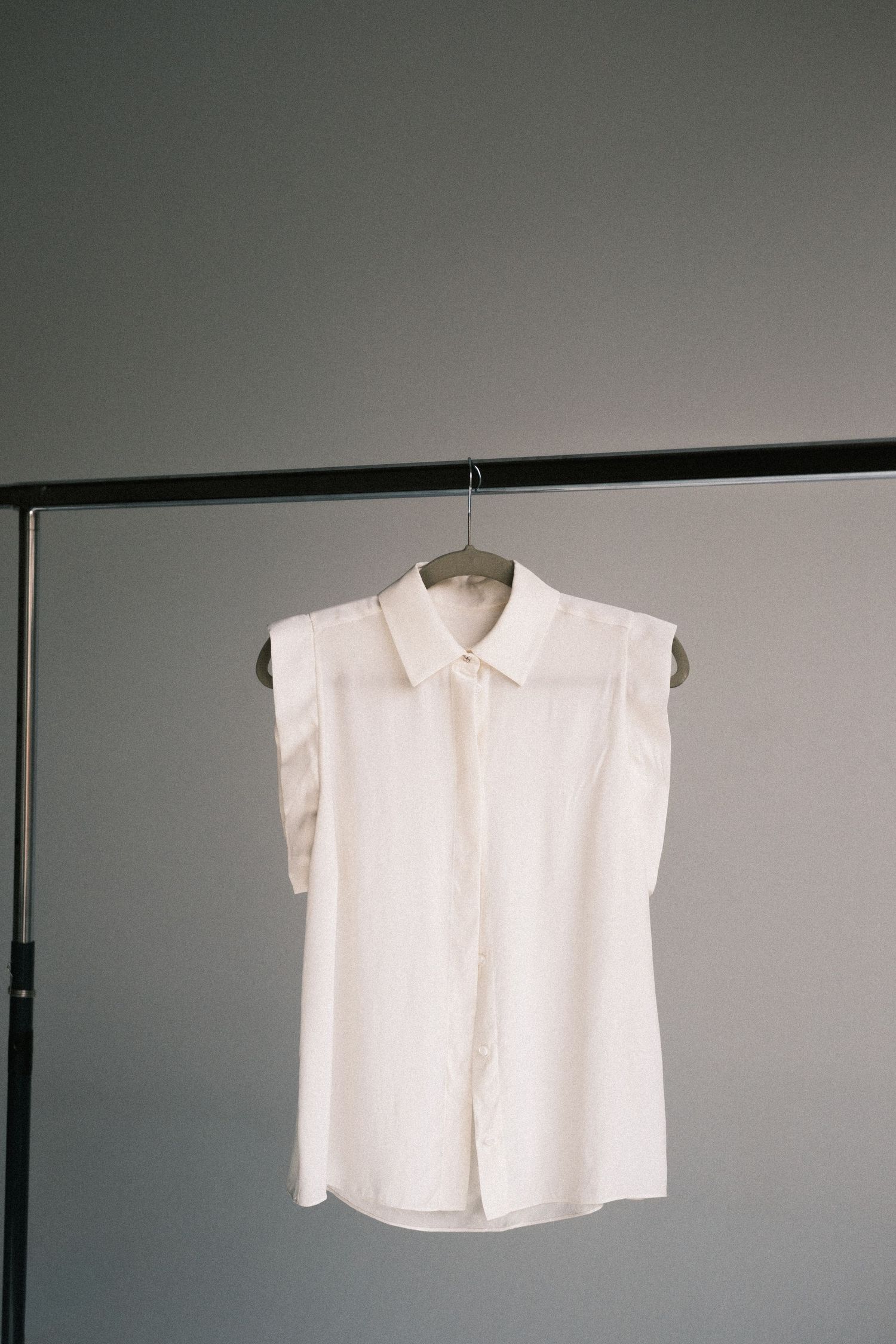 A minimalist white button-up shirt hangs against a gray wall in a sequence of similar views.