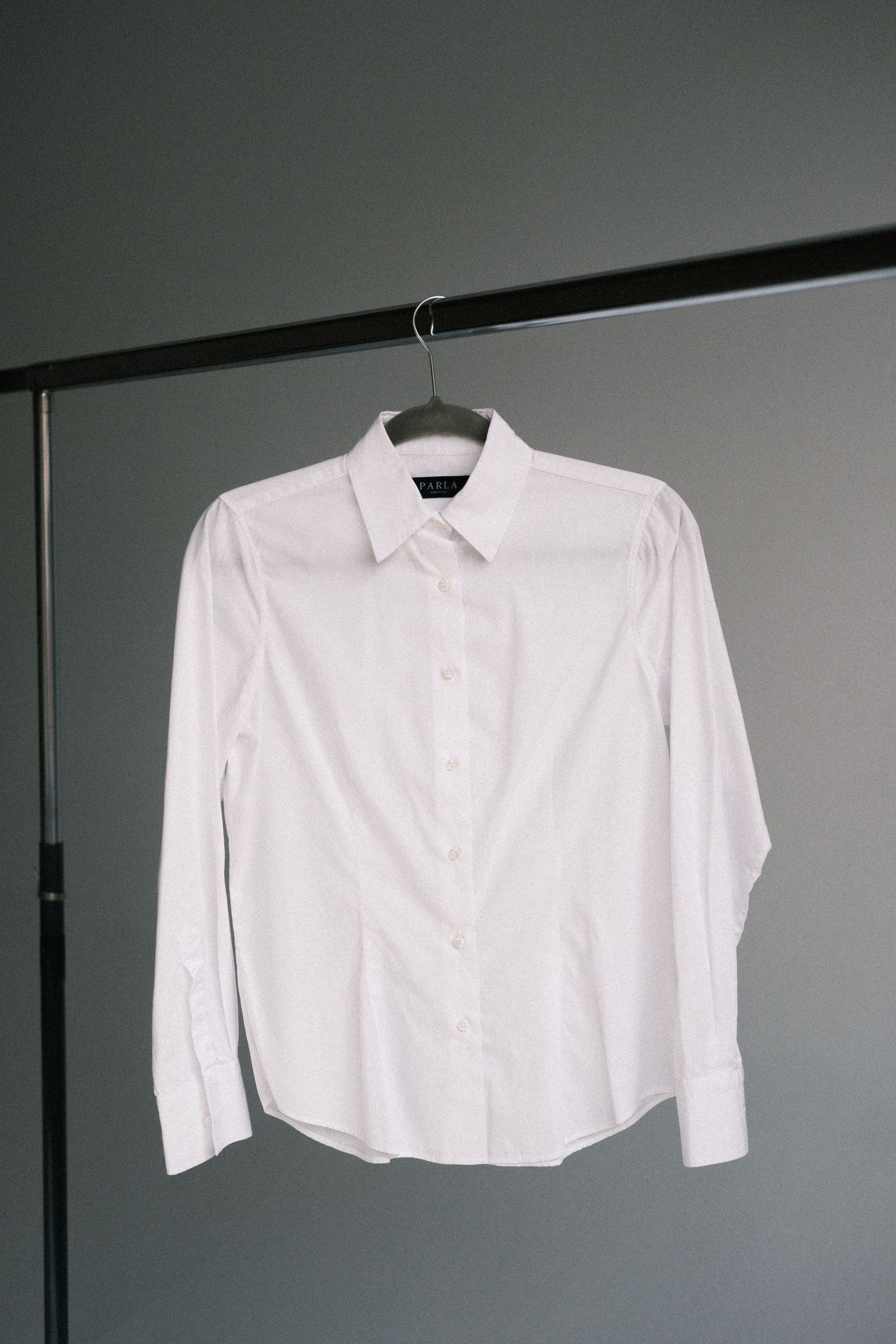 A series of white button-down shirts hanging on a clothing rack against a gray wall.
