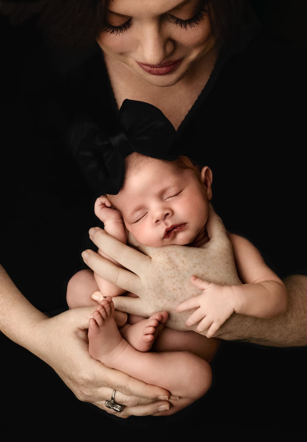 New mom cradles her sleeping baby girl against a warm black backdrop, captured by Charlottesville newborn and family photographer.