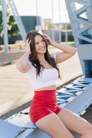 A person in a white top and red shorts poses on bleachers during a summer photoshoot.