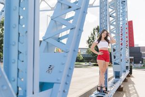 Person in red shorts stands near a geometric blue metal structure on a sunny day by the waterfront.