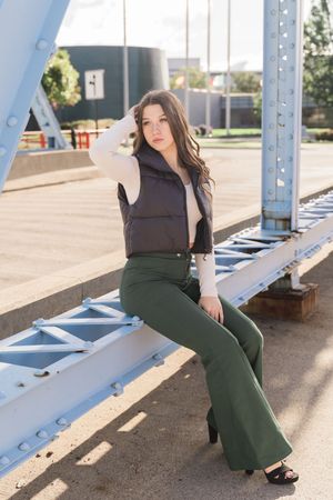 Fashion model poses in an elegant green dress and black top against industrial metal beams in natural lighting.