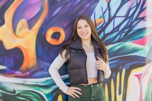 Woman poses in front of vibrant street art mural featuring colorful abstract designs and patterns.