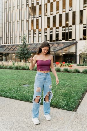 Stylish outfit featuring distressed blue jeans and a burgundy crop top paired with white sneakers on a sunny day.