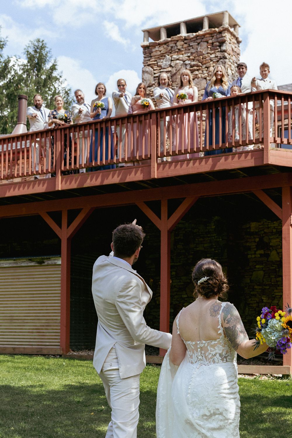 Wedding party gathers on rustic wooden deck for group photos during outdoor celebration.