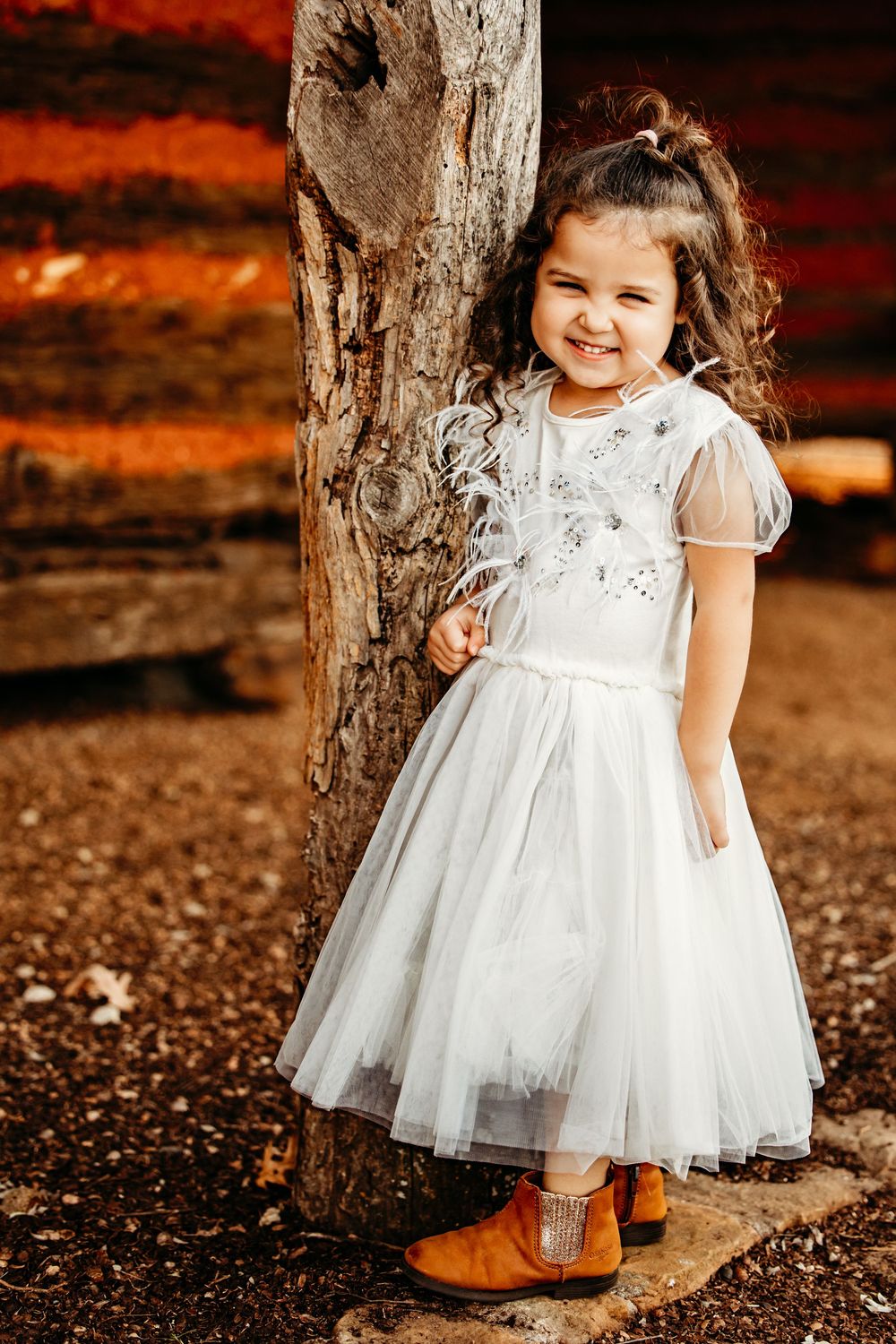 A white lace tulle dress with cap sleeves paired with brown boots stands out against a rustic autumn background.