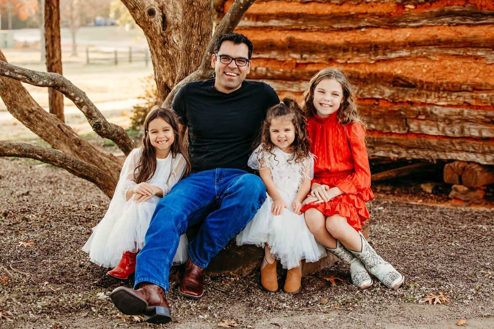 Family sits together on fallen tree trunk surrounded by autumn foliage in outdoor photo session.