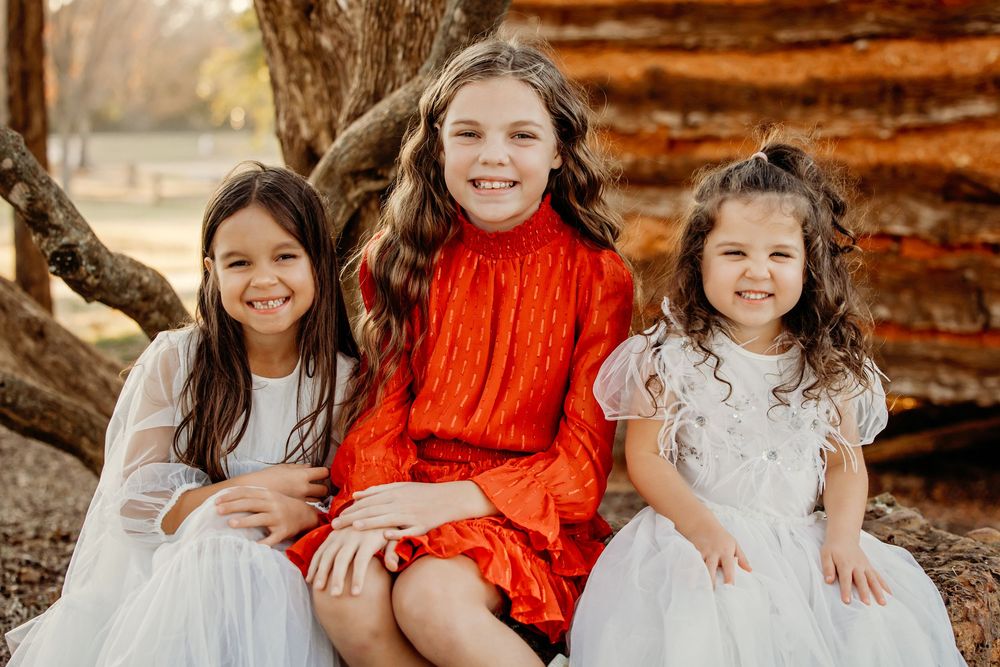 A group of children sit together wearing coordinated orange and white outfits during an autumn outdoor photo session.