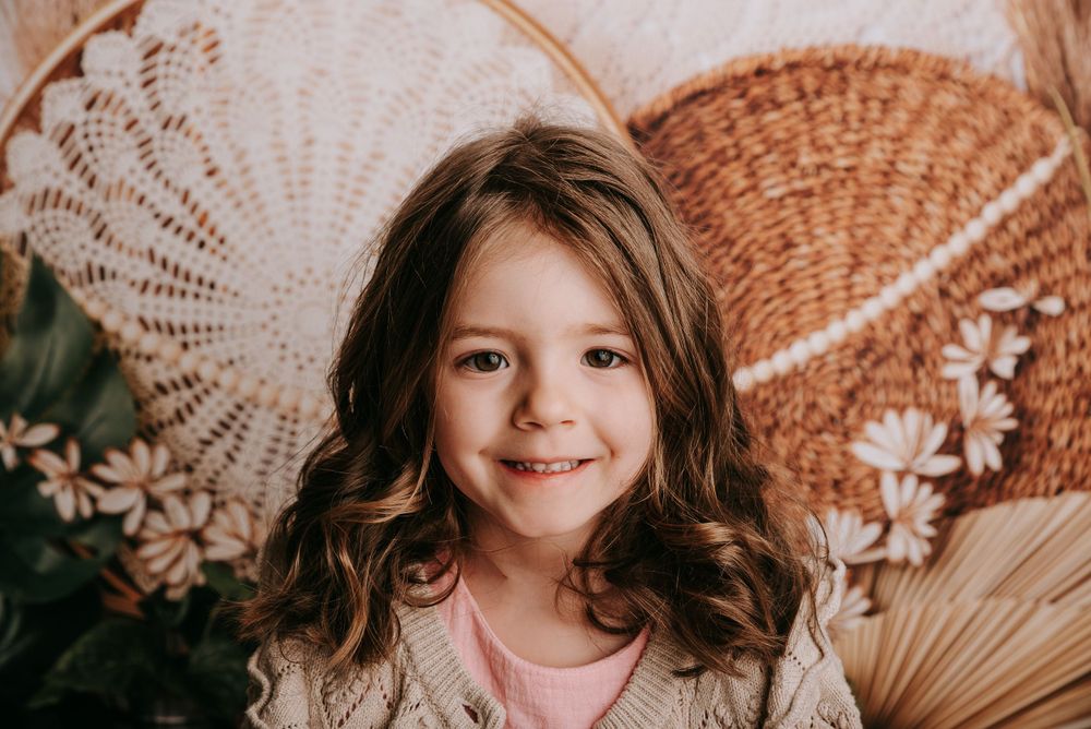 Portrait of child wearing pink against natural boho background with woven baskets and dried flowers.