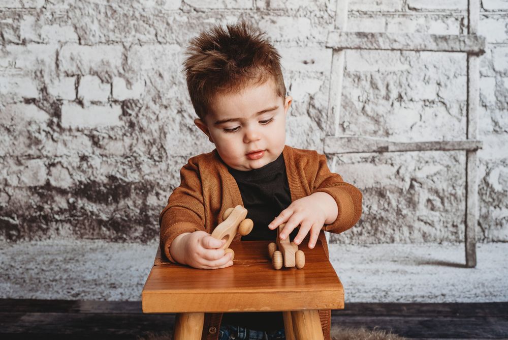 Child in brown sweater playing with wooden toys at small table against brick wall.