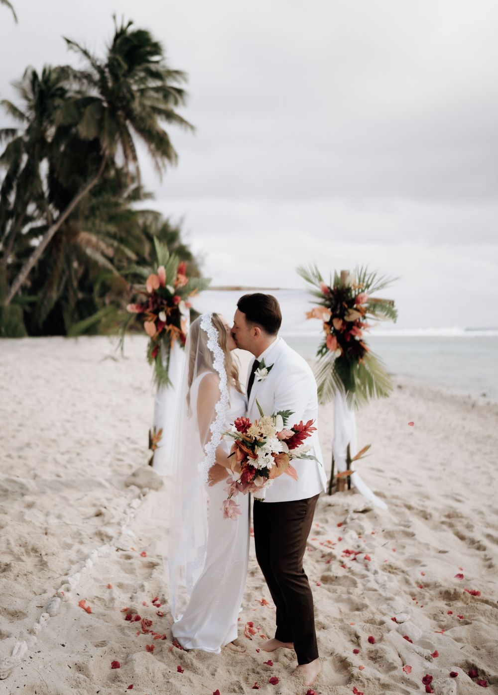 A romantic beach wedding scene with palm trees swaying in the wind as a couple shares a tender moment on the sandy shore.