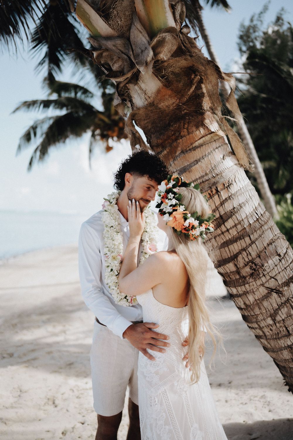 A couple embraces on a tropical beach with palm trees and soft sunlight creating a romantic wedding scene.