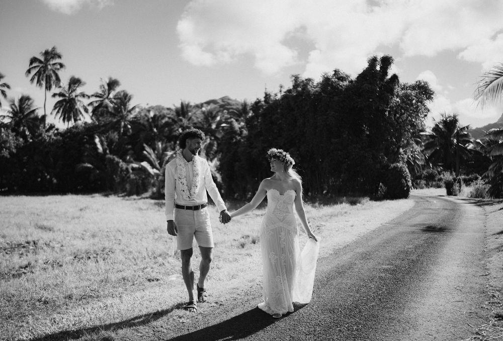 A couple walks hand in hand down a tropical road lined with palm trees in black and white.