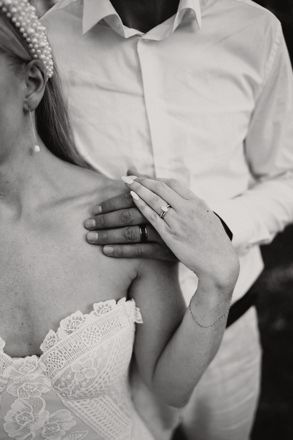 Black and white close-up of newlyweds embracing, showing wedding rings and delicate lace bridal gown details.