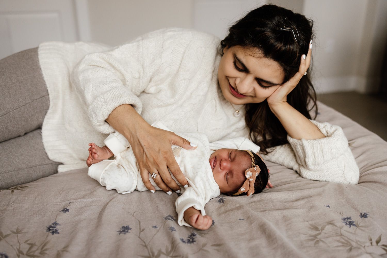 A mom smiles at her sleeping newborn baby