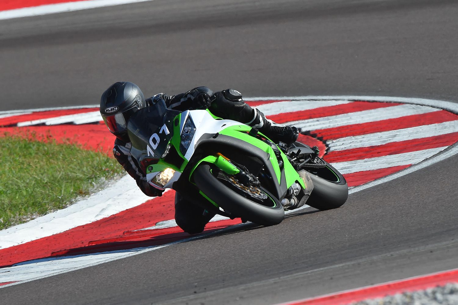 Motorcycle racing on a racetrack with red and white curbing at high speed.