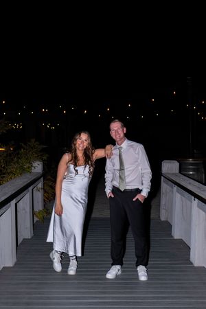 A couple in wedding attire sits and laughs together on outdoor steps at night.