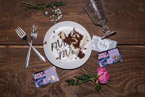 Chocolate dessert plate with scattered crumbs and decorative greenery on rustic wooden table.