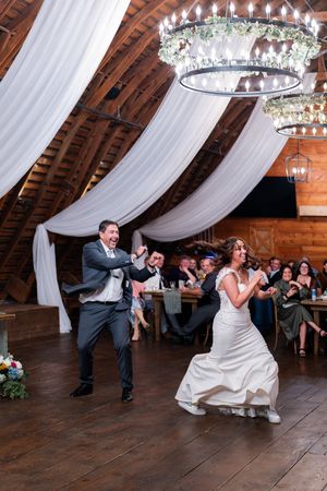 Wedding party performs synchronized dance move by leaning to the side during a reception in a rustic barn venue.
