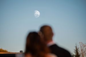 A couple gazes at the moon in the blue sky during a romantic moment.