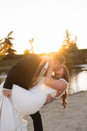A romantic sunset beach scene shows a couple in wedding attire sharing a dramatic dip pose by the water.