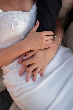 Close-up view of hands with wedding rings resting on white fabric showing romantic details of a wedding ceremony.