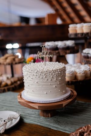 White wedding cake with delicate pearl decorations displayed on wooden cake stand against rustic background.