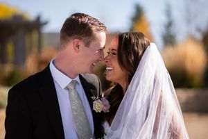 A romantic wedding couple shares an intimate moment in golden sunlight with autumn trees in the background.