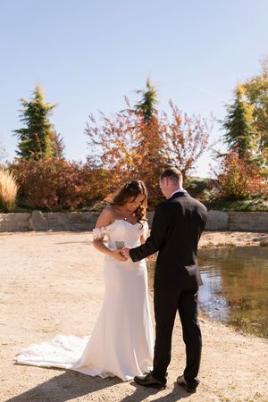 A wedding couple walks together on a stone path near a pond surrounded by fall foliage.