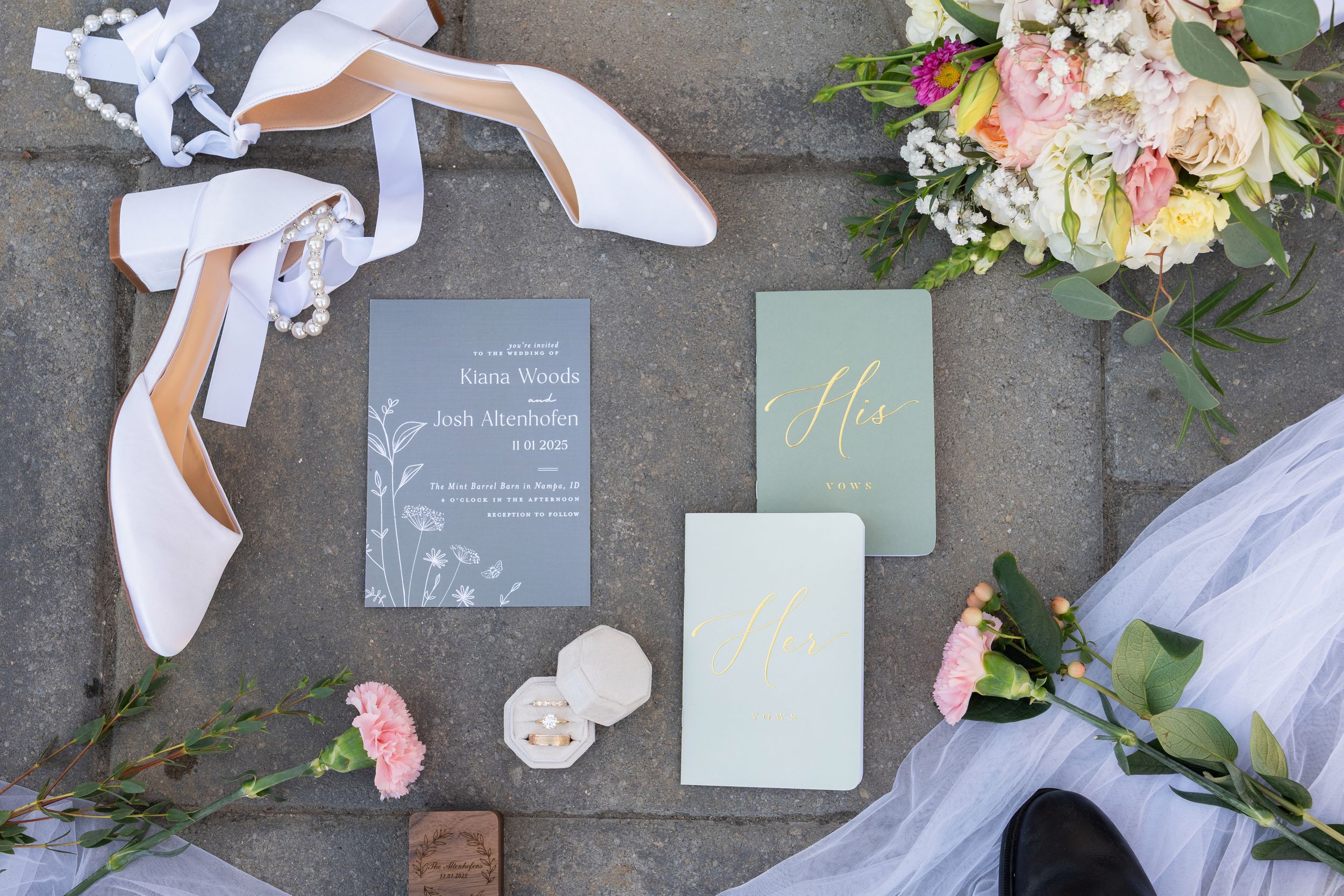 A wedding flatlay with white shoes, floral bouquets, and gray invitation cards arranged on a stone surface.