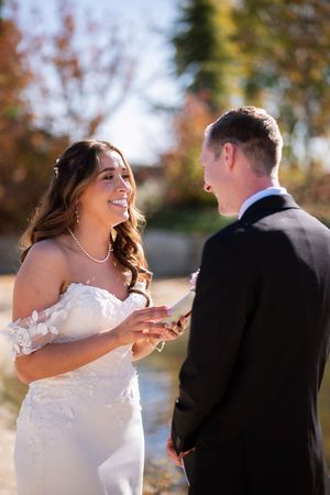A couple laughs together during their outdoor fall wedding celebration with golden foliage in the background.