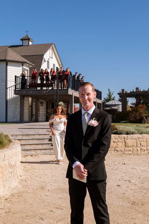 Wedding couple poses for photos on stone steps outside a white building with onlookers visible on the balcony.