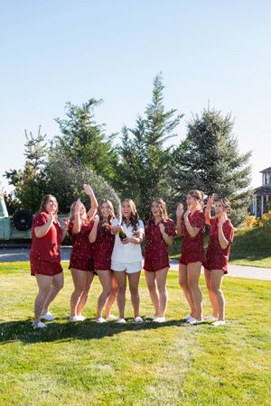 A group in burgundy outfits poses together on a sunny lawn, showing excitement and joy.