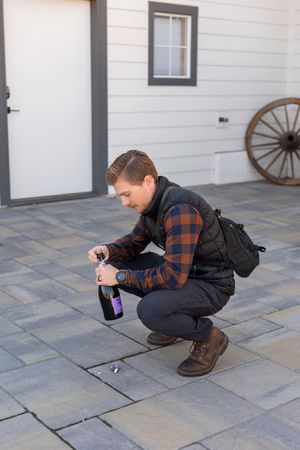 Person in plaid shirt and backpack crouches down to take photos of something on stone pavement.