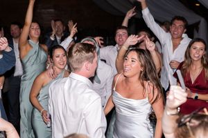 Wedding reception guests dancing and celebrating on a crowded dance floor with hands raised in excitement.