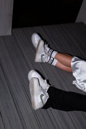 A sequence of white sneakers with green accents shown from different angles on a gray wooden deck.
