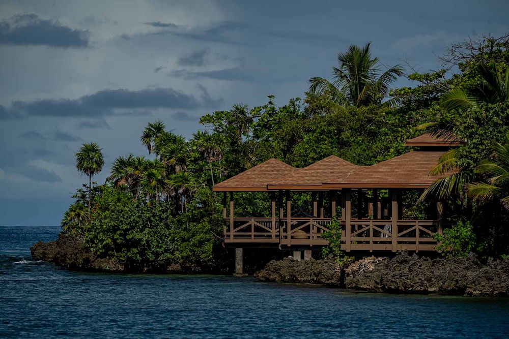 A series of wooden bungalows nestled along a tropical coastline with palm trees and turquoise waters.