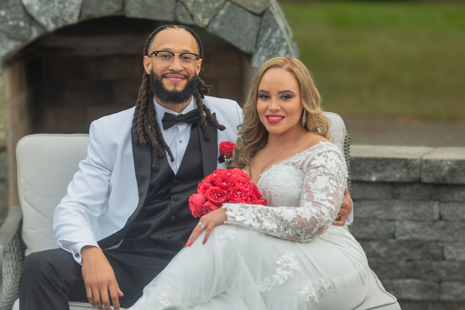A wedding couple sits together on stone steps in a garden setting during their outdoor photoshoot.